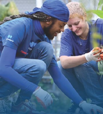 A man and woman wearing BlueCrew t-shirts smile as they volunteer together in a community garden. A man and woman wearing BlueCrew t-shirts smile as they volunteer together in a community garden.