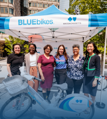 Group photo of Blue Cross CEO Sarah Iselin, Boston Mayor Michelle Wu, and others smiling as they stand outdoors behind a Bluebikes e-bike Group photo of Blue Cross CEO Sarah Iselin, Boston Mayor Michelle Wu, and others smiling as they stand outdoors behind a Bluebikes e-bike