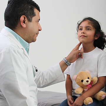 Image of a male pediatrician checking the pulse of a girl patient holding a teddy bear in an examination room Image of a male pediatrician checking the pulse of a girl patient holding a teddy bear in an examination room